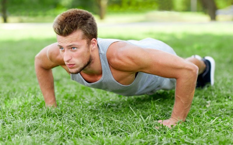 fitness, sport, exercising, training and lifestyle concept - young man doing push ups on grass in summer park